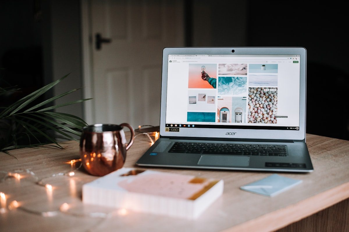 Laptop on a warm-lit desk displaying a moodboard of layouts alongside a copper mug