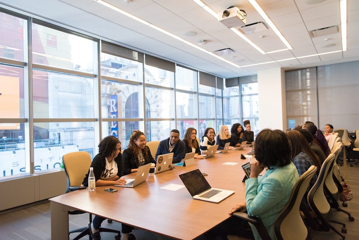 Sunlit boardroom of decision-makers reviewing content on laptops around a long conference table